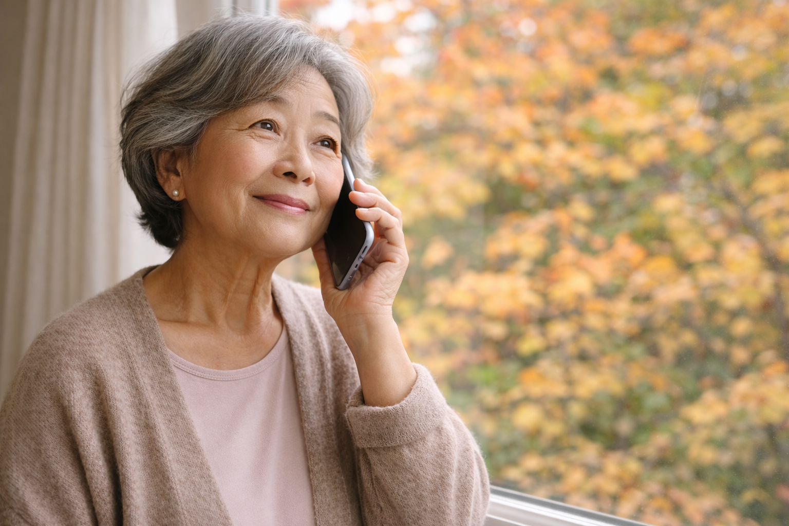 Woman chatting on phone by a window with autumn foliage